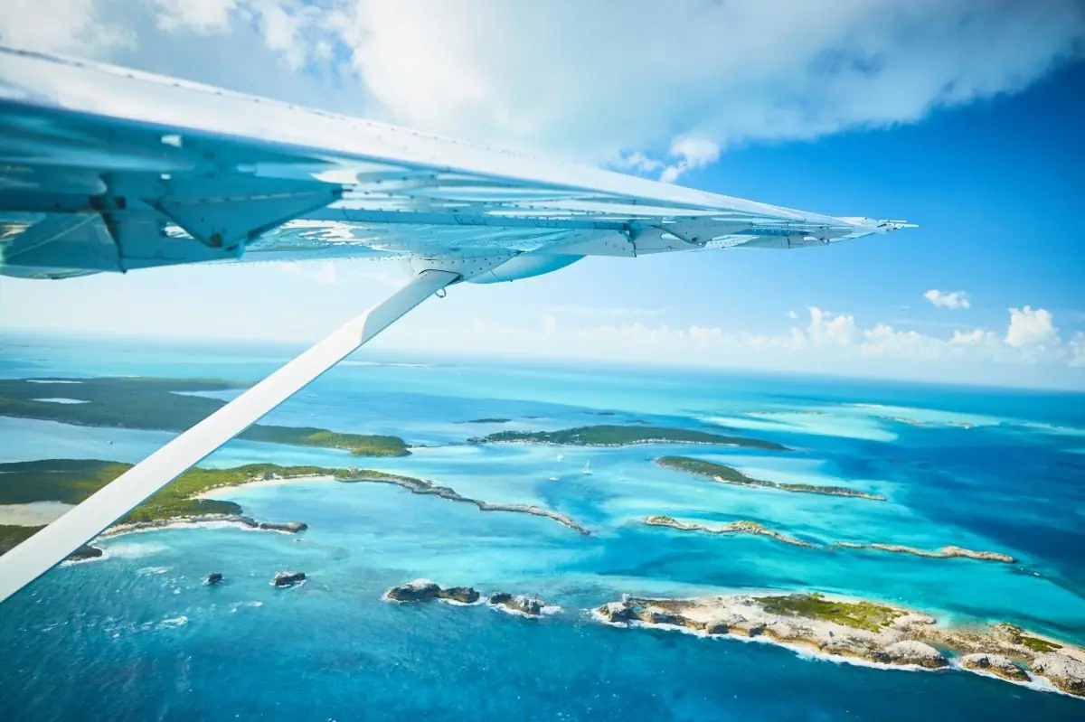 View from a small plane window on approach to Staniel Cay, with turquoise shallows and small islands below.
