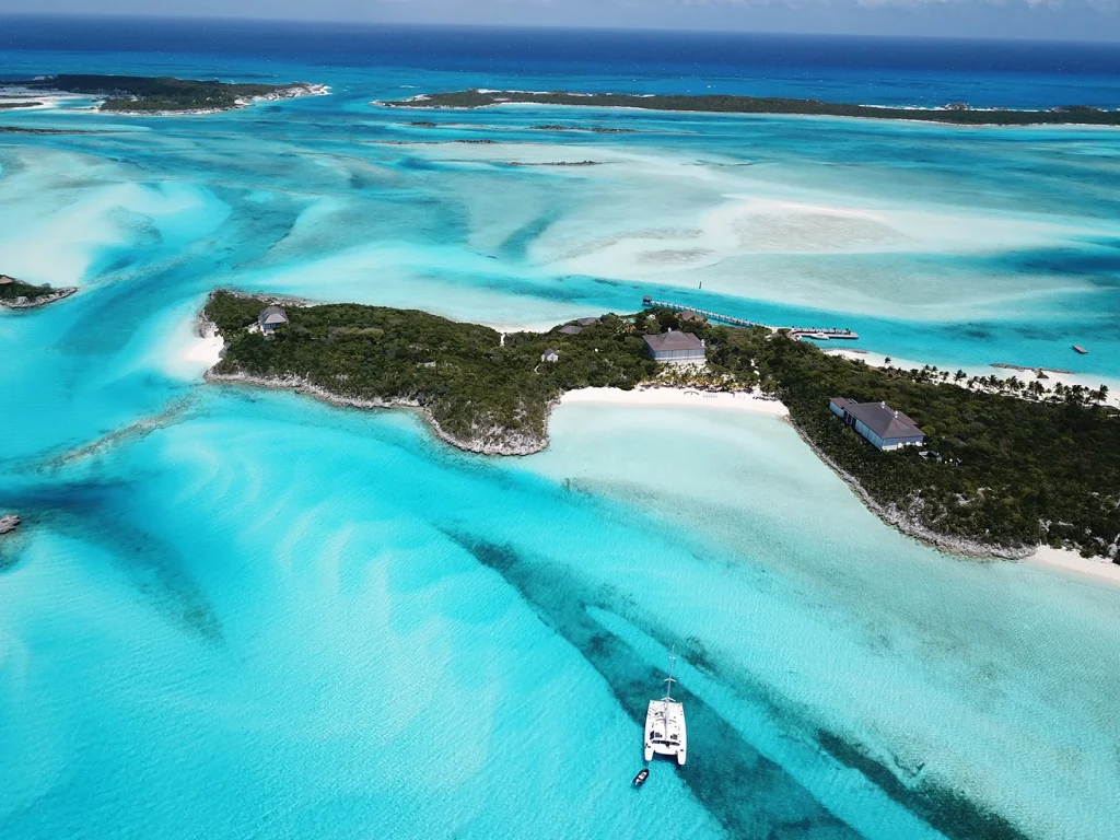 Aerial view of a turquoise lagoon with small islands and a catamaran anchored nearby.